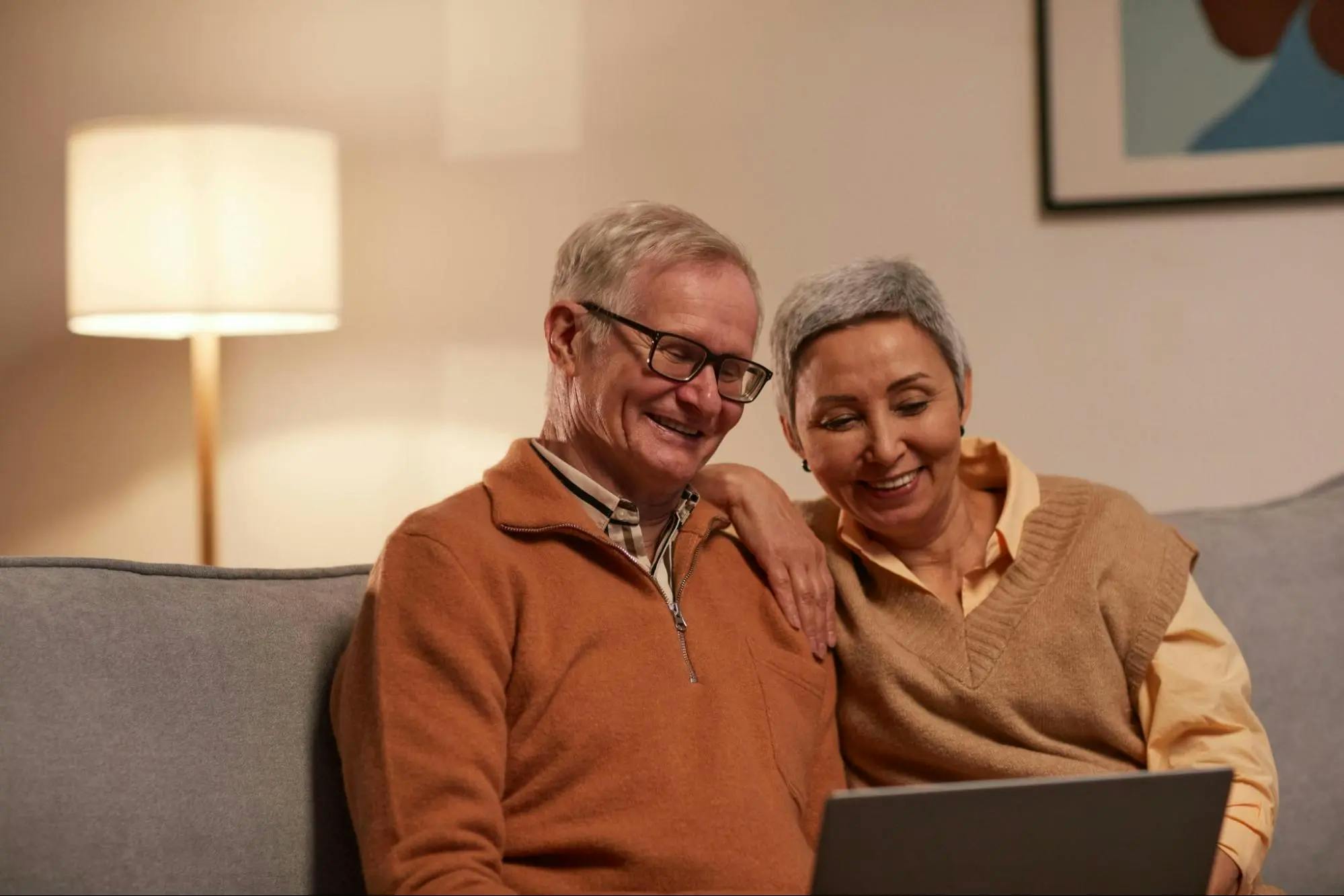 An elderly couple sitting on the couch, using a laptop together