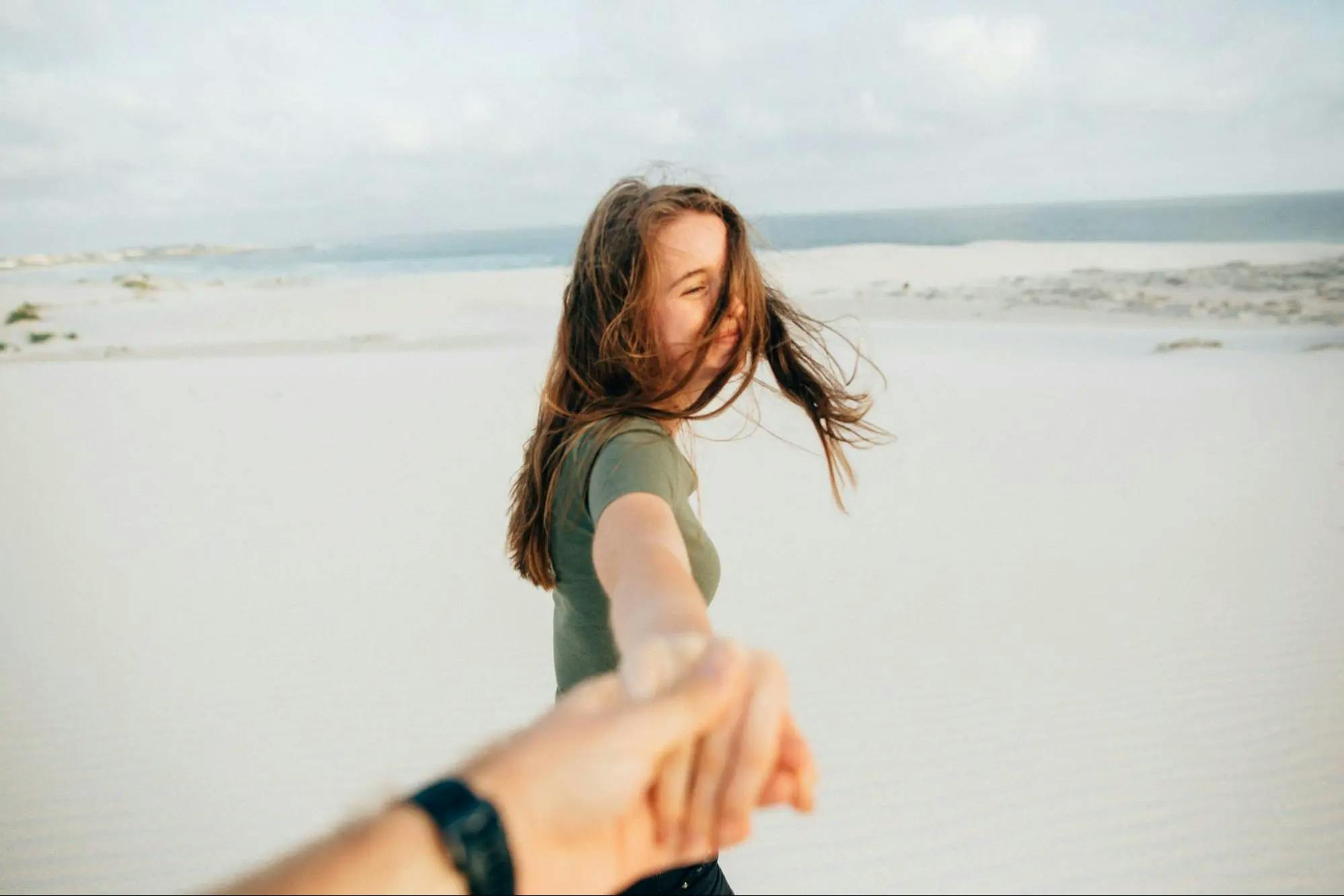 A happy girl holding hands with her boyfriend on a sandy beach