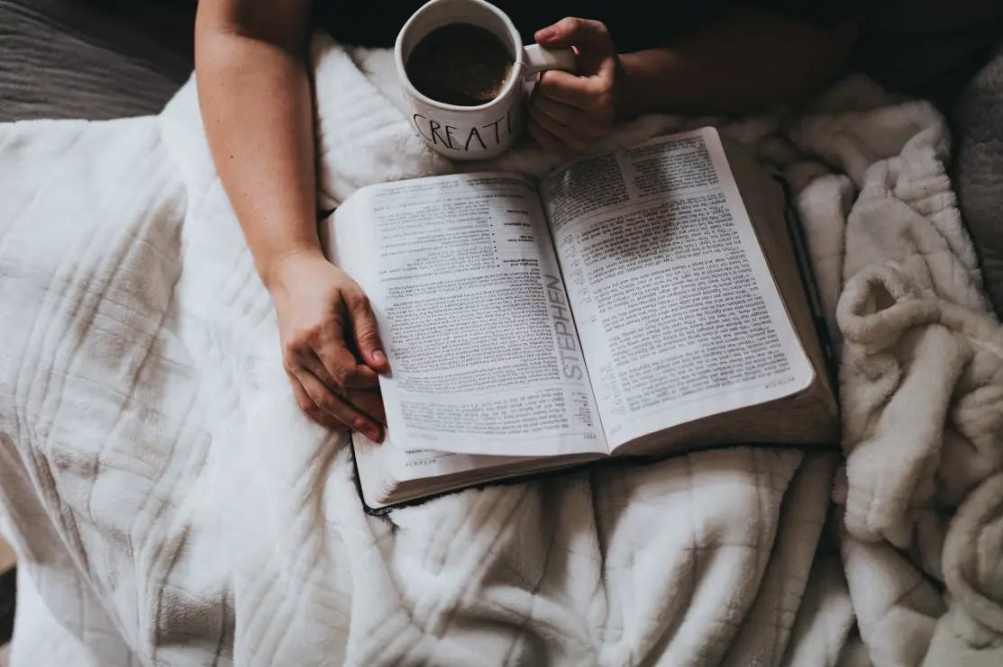 Person reading in bed while drinking a cup of coffee