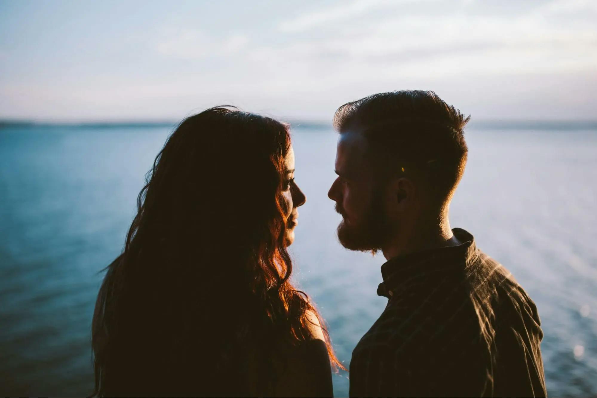 Couple standing by the sea, gazing into each other's eyes.
