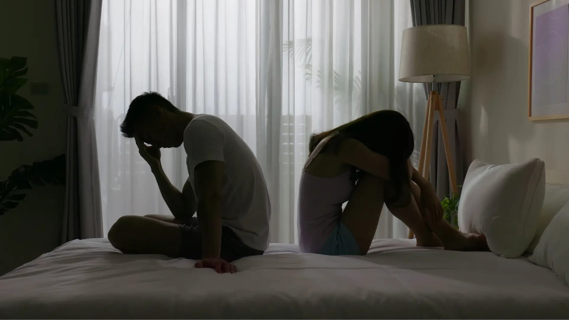 Couple sitting on the bed with their backs turned to each other