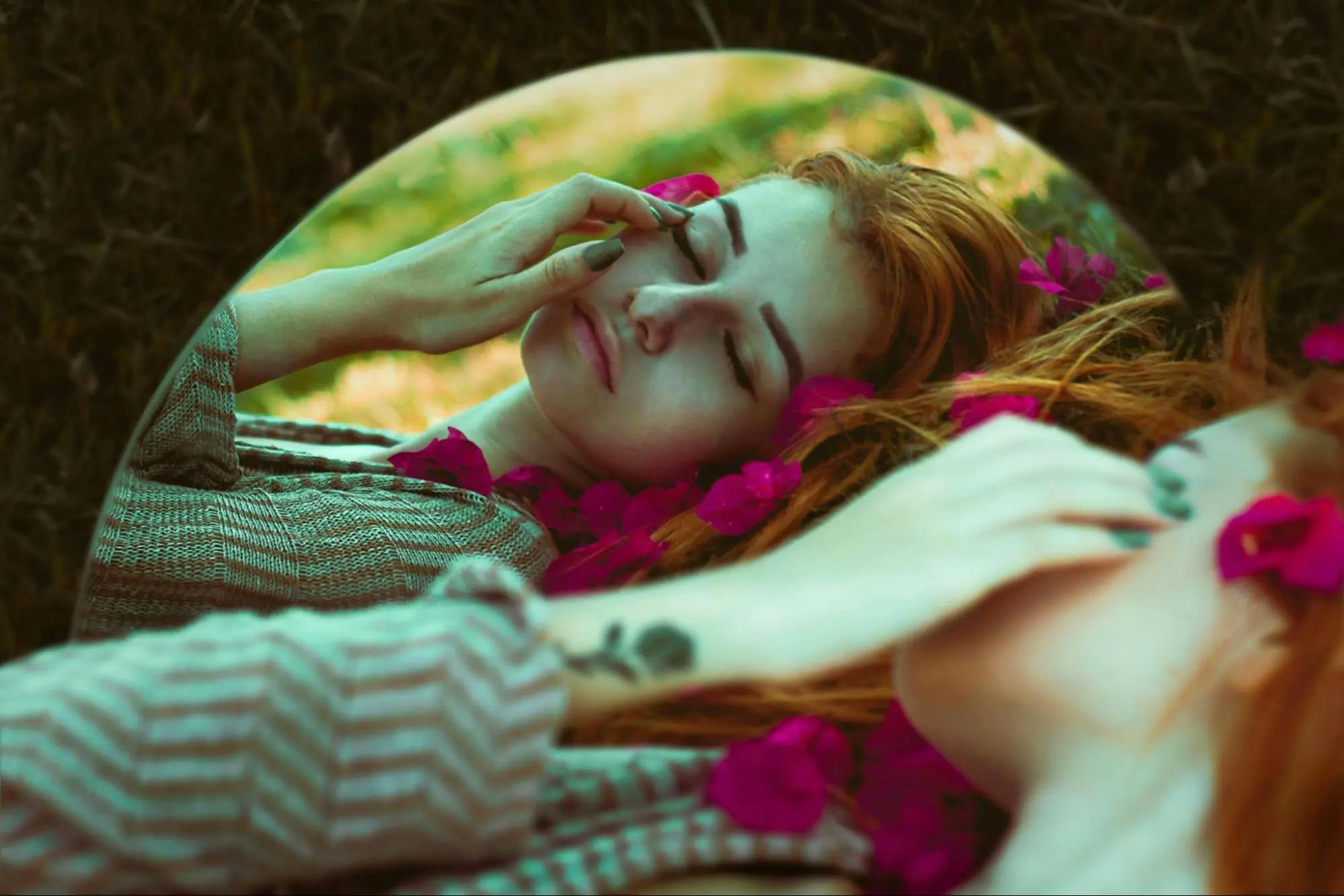 A woman's reflection in a mirror lying on the grass, surrounded by purple flowers