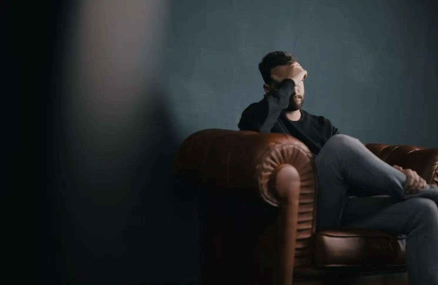 Man sitting in a chair, looking stressed.