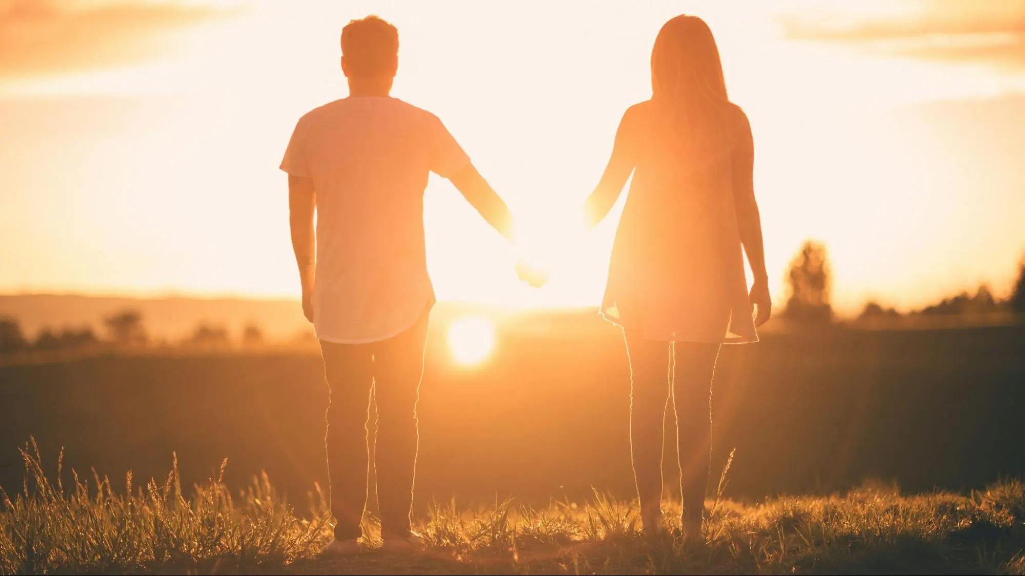 Couple standing hand-in-hand, facing the sunset